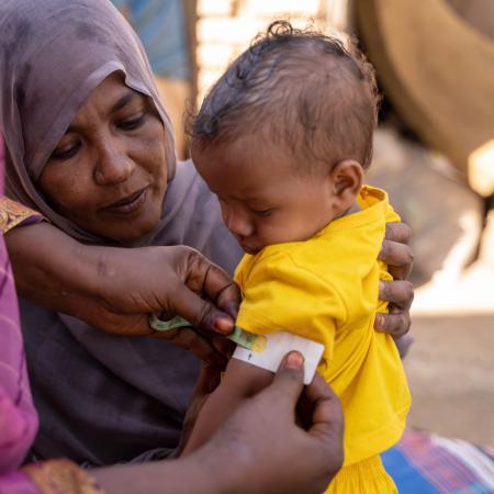 Une membre d’un groupe de soutien aux mères au Soudan fait passer un test de dépistage de la malnutrition à Fatuma, âgée de 9 mois, dans les bras de sa mère.