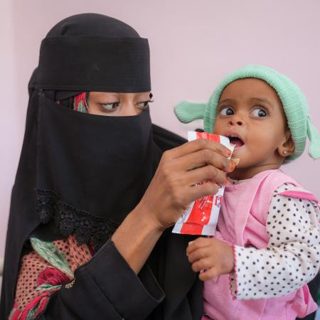 On 23 February 2023 in Aden, Yemen, 16-month-old Rowaida Raeed Ali Hasan is fed a sachet of Plumpy ‘Nut ready-to-use therapeutic food (RUTF) by her mother, Gouma’a Mohammed Hasan Abdullah. Rowaida is being treated for severe acute malnutrition in the Therapeutic Feeding Centre at Al Sadaqa Hospital.