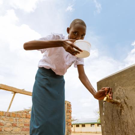Teenage girl sips water while smiling at the camera in Kenya.
