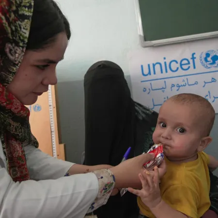 A health worker feeds a child ready-to-eat therepeutic food while his mother holds him 