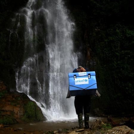 A vaccinator climbs a rocky path.