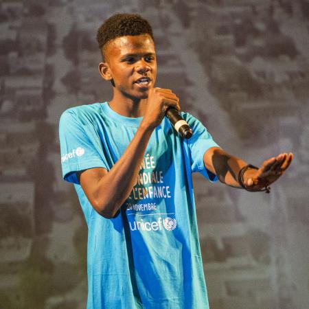 Teen boy holding microphone where World Children's Day cyan blue shirt