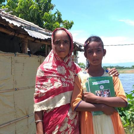 A woman and her daughter stand outside a makeshift home in Bangladesh.