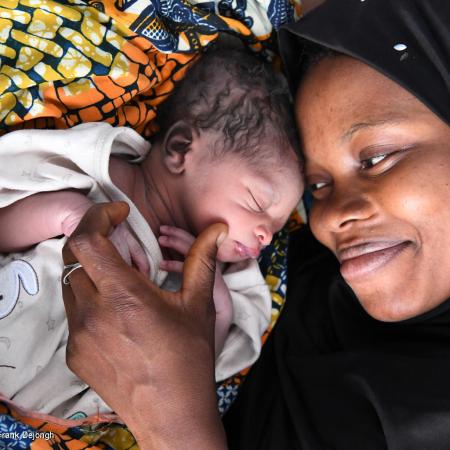 A women looks at her new born child smiling, the child's eyes are closed. This photo was taken in Odienné, in the Northeast of Côte d'Ivoire 