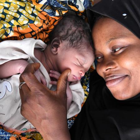 A women looks at her new born child smiling, the child's eyes are closed. This photo was taken in Odienné, in the Northeast of Côte d'Ivoire