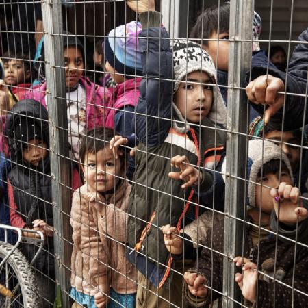 Children wait in a crowded processing area for refugees.
