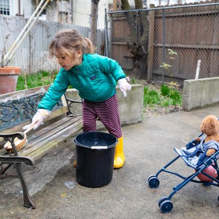 A little girl cleans her play area with soap and water.