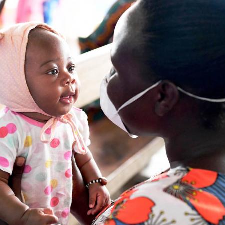 Staring amused at her mother's mask covered face, 3-month-old Christelle