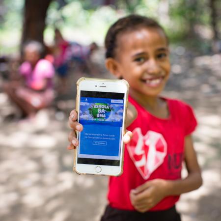Child in Timor-Leste holding up cell phone with the Learning Passport on the display