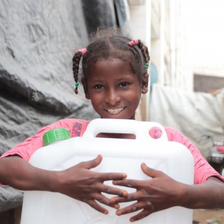 A little girl holds a jerry can of clean water.