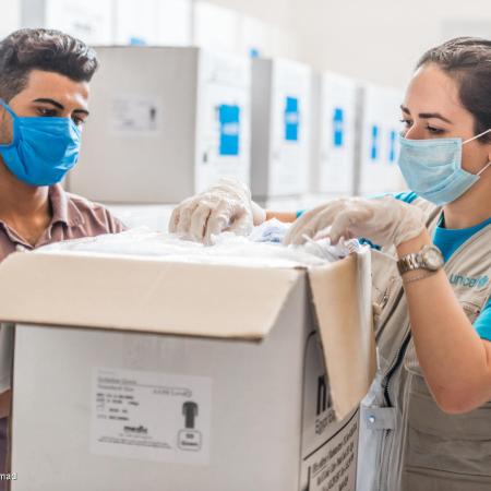 A man and a woman pack up a box of vaccines. They are both wearing masks and the woman is wearing a UNICEF vest.