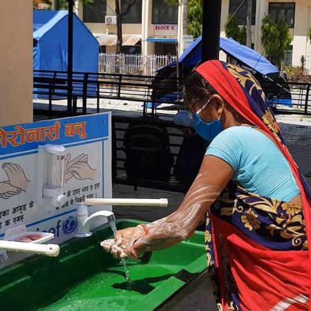 A woman washes her hands at a portable washing station.