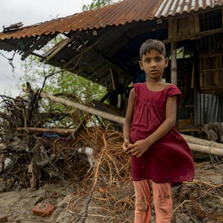 A child stands in front of her tin house in Bangladesh.