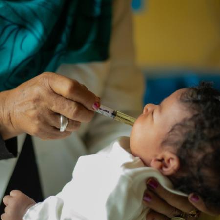 A hand administers a vaccine to a baby, using a plastic syringe.