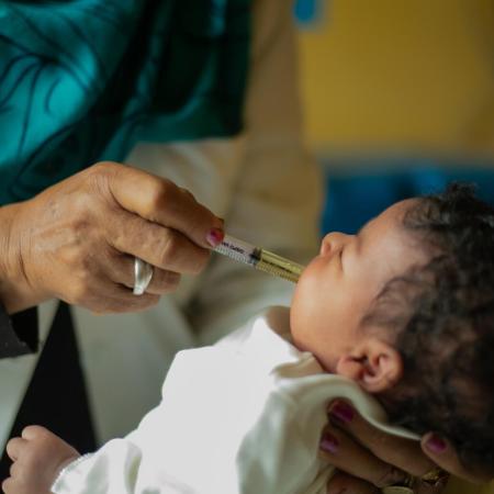 Une main administre un vaccin oralement à un bébé, en utilisant une seringue en plastique.