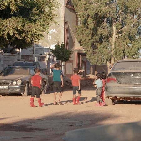 Young children are walking around in the neighborhood in boots despite the hot weather because they still worry about the floods and drowning, they have been displaced to a whole new city that they are still trying to familiarize themselves with.