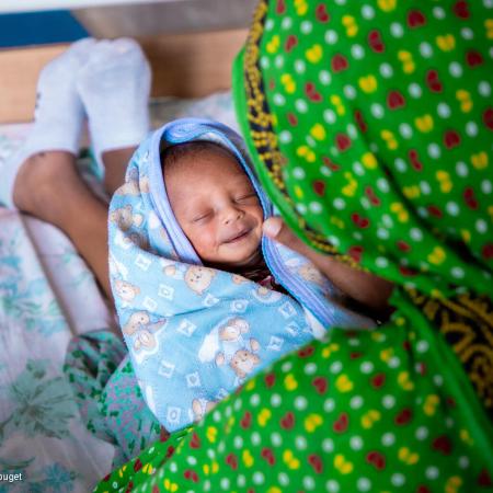 Un bébé enveloppé dans une serviette sourit sur les genoux de sa mère.