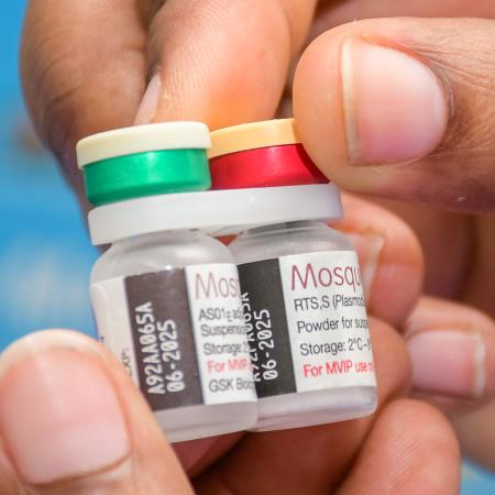 A close up shot of a hand holding two vials of the malaria vaccine