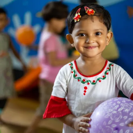 A young girl holds a ball and smiles for a photo. 