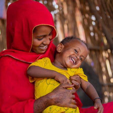 A mother holds her child lovingly as it laughs in her lap. 