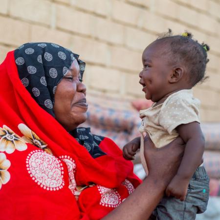 Au Soudan, une mère souriante tient dans ses bras sa fille âgée de 10 mois.