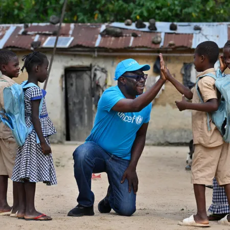 Un employé de l’UNICEF tape dans la main d’un jeune garçon tandis que d’autres enfants se tiennent autour d’eux.