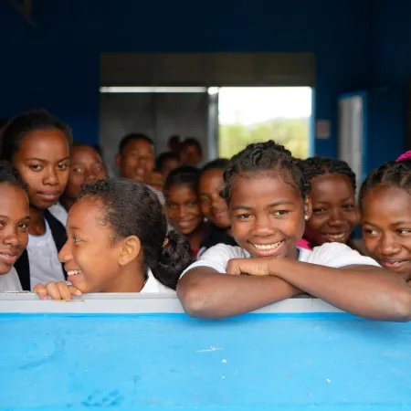 A group of young girls smile and look out from a window.