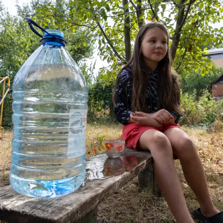 A girl is sitting n a bench next to the bottle of clean water.