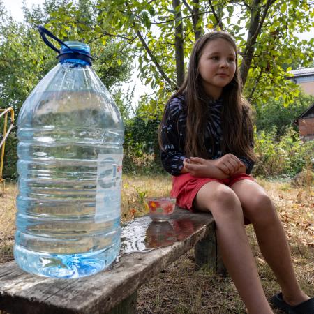 A girl is sitting n a bench next to the bottle of clean water.