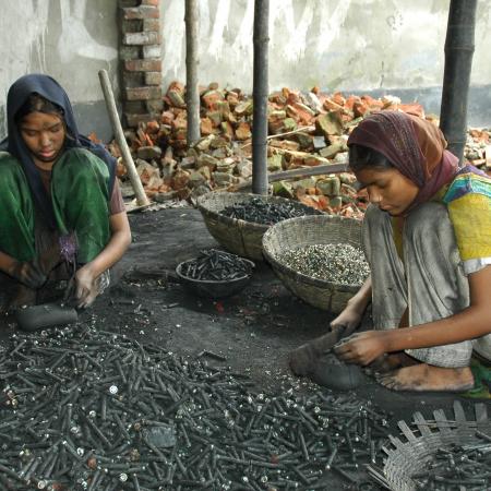 Two girls break used batteries to get pieces of metal out of them for recycling.