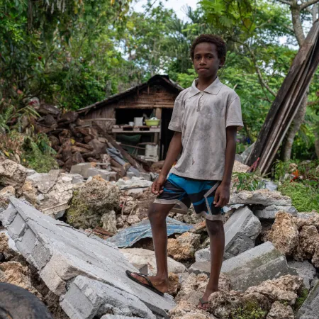 A boy stands in front of rubble.