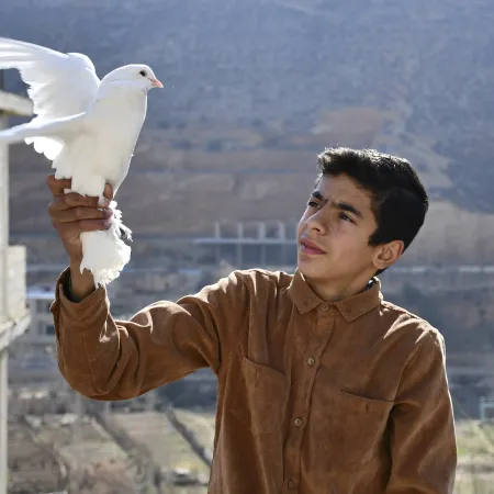 Mohammed, 15, gently holds a bird he has raised on the roof of his home in Bseimeh village, Rural Damascus, Syria