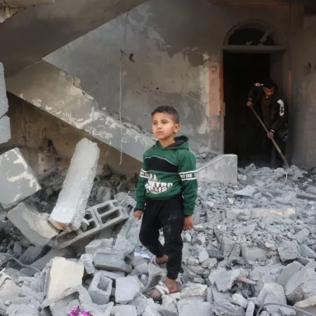 A young boy walks through rubble, surrounded by destruction and debris. 