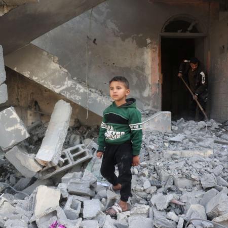 A young boy walks through rubble, surrounded by destruction and debris.