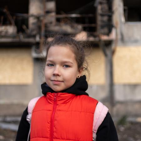 Eight-year-old Myroslava stands in front of a bombed-out residential building, one of several damaged in a missile strike on 7 March in Eastern Ukraine.