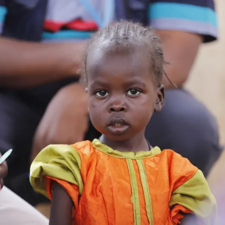 A child looks on as health workers screen children for malnutrition at a UNICEF-supported Primary Health Clinic in Tawila, North Darfur, Sudan