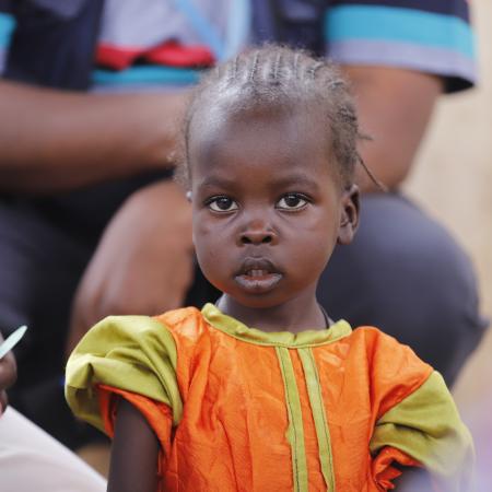 A child looks on as health workers screen children for malnutrition at a UNICEF-supported Primary Health Clinic in Tawila, North Darfur, Sudan