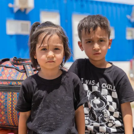 In an outdoor setting, a boy and a girl sit next to their luggage.