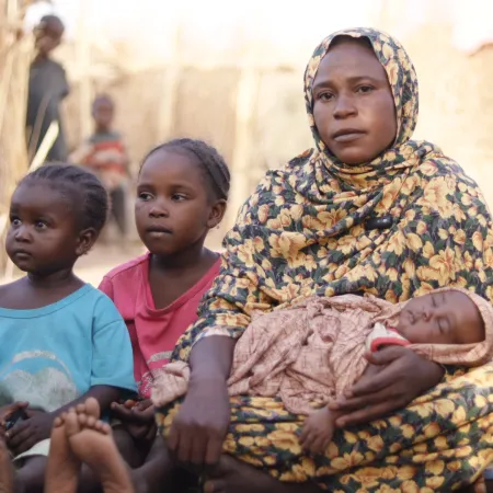 Amani carries her newborn baby next to her makeshift shelter in Tawila where she fled with her family after intensified fighting back home in Al Fasher, North Darfur.