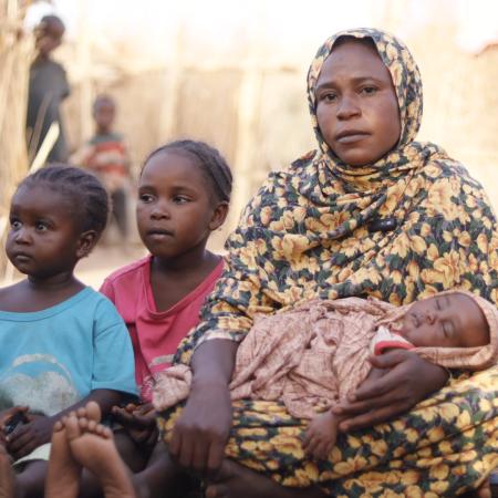 Amani carries her newborn baby next to her makeshift shelter in Tawila where she fled with her family after intensified fighting back home in Al Fasher, North Darfur.