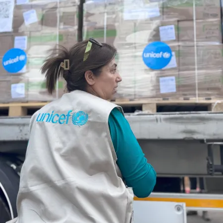 Woman wearing a UNICEF vest standing in front of UNICEF supply truck.