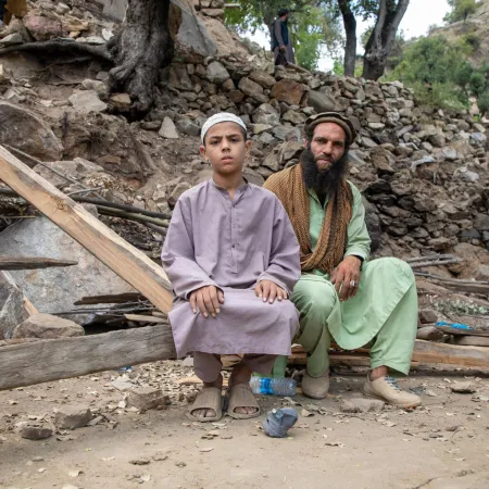 A man and a child sit in front of rubble.