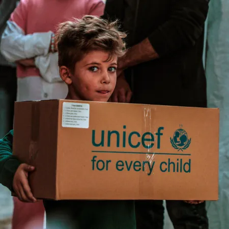 Un enfant portant une boîte au logo de l’UNICEF regarde l’objectif.