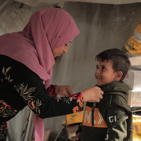 A smiling child looks up at his mother as she helps him put on a warm jacket.