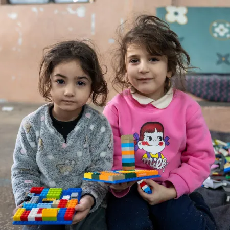 Dans un refuge, deux enfants assis par terre tiennent des créations Lego colorées.