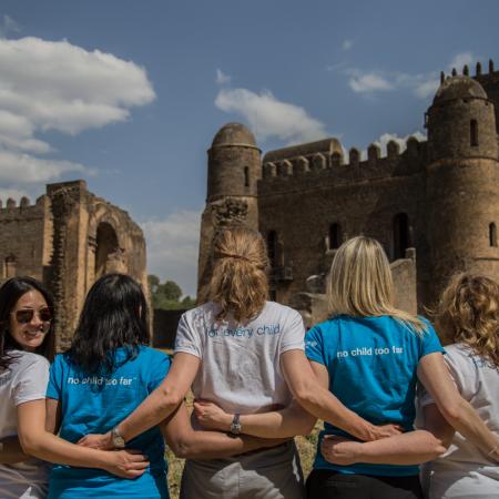Un groupe de cinq femmes photographiées de dos forment une ligne, l’une d’entre elles tournant le regard vers l’arrière et souriant à l’objectif.