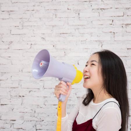 Smiling teen girl holding megaphone in front of a white brick wall