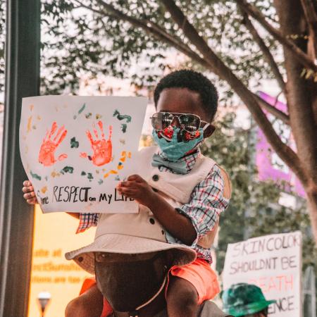 A child sits on a man's shoulders holding a protest sign.