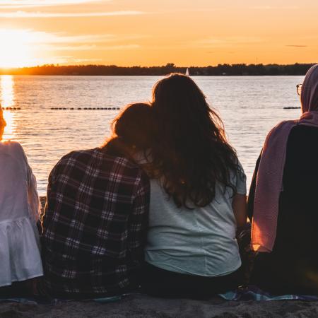 A group of young girls sit facing a sunset.