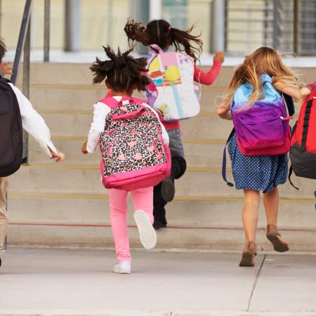 Kids wearing backpacks running into school